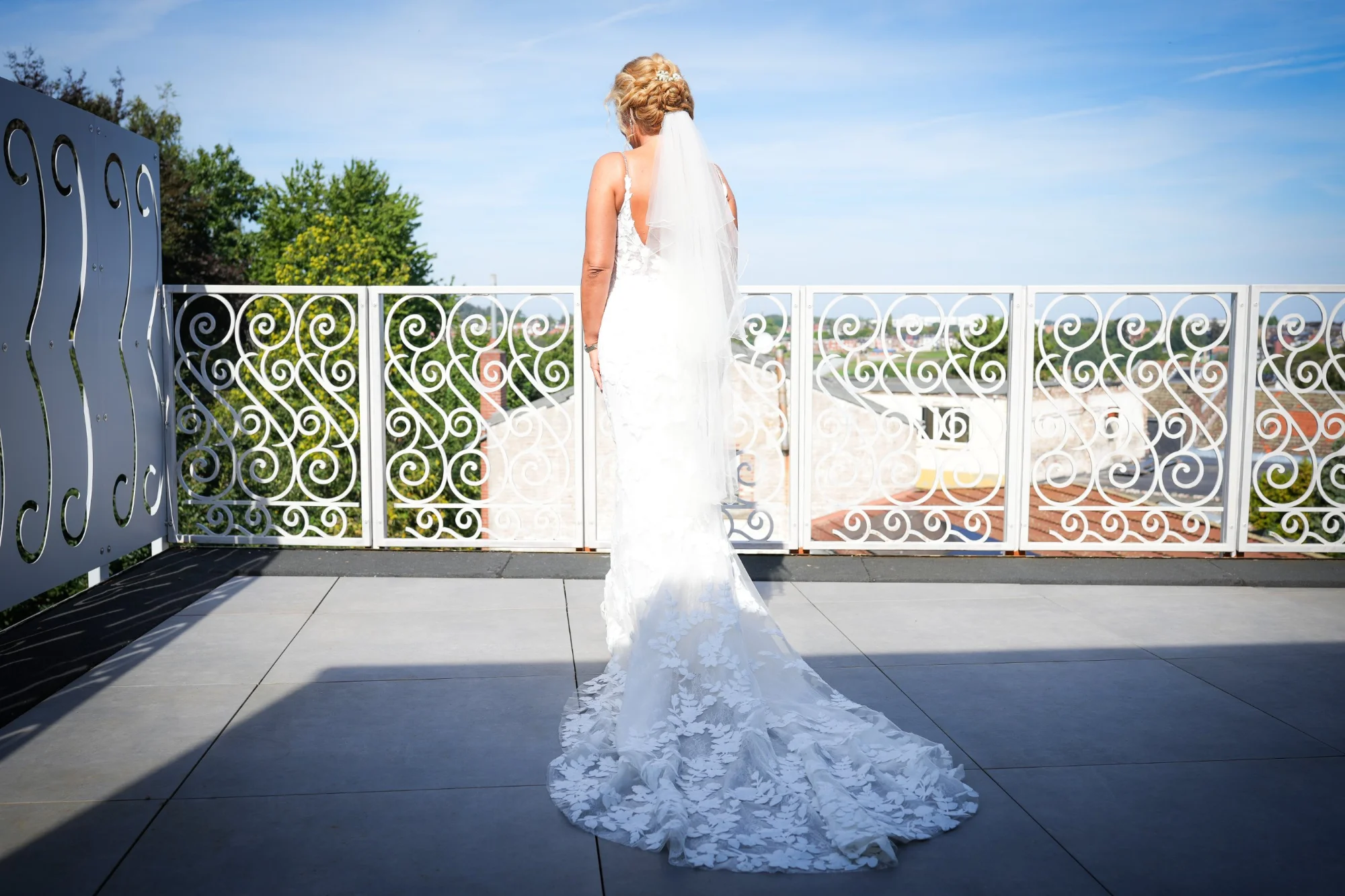 La mariée de dos sur une terrasse, sa traîne en dentelle étalée au soleil