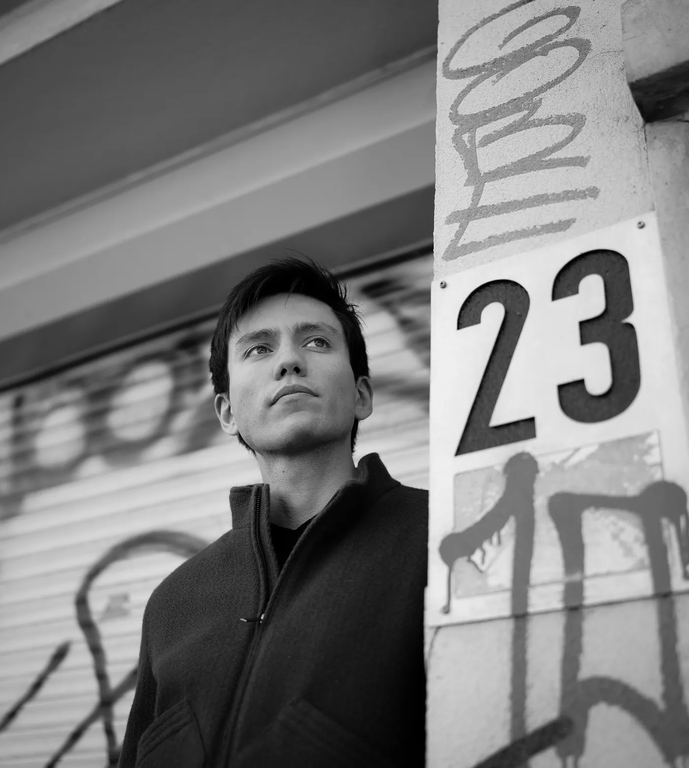 Portrait en noir et blanc, regard au loin, devant un rideau de fer tagué